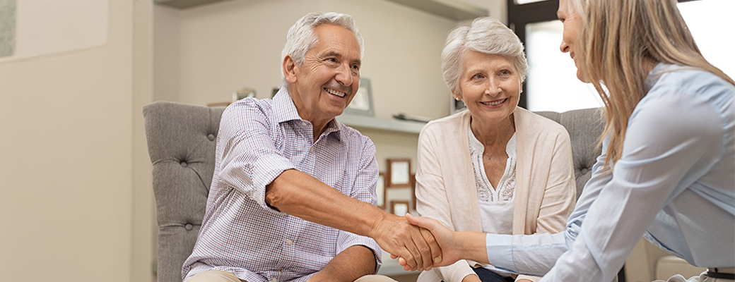 Image of senior man shaking hands with a hearing care professional beside his wife 